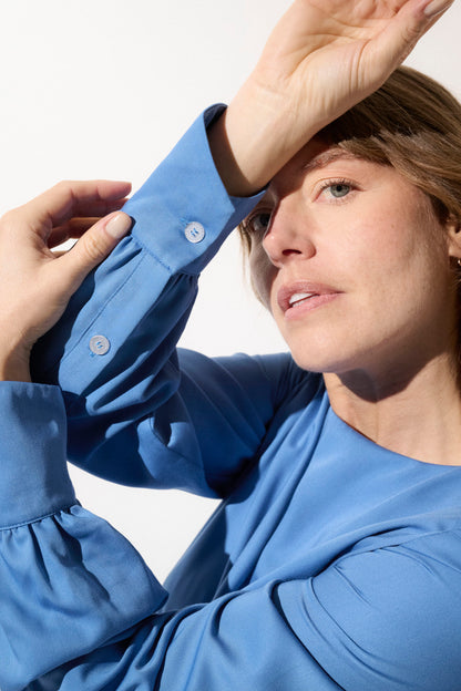 Femme portant une blouse bleue élégante, protection solaire anti-UV et confort, idéale pour les journées ensoleillées.