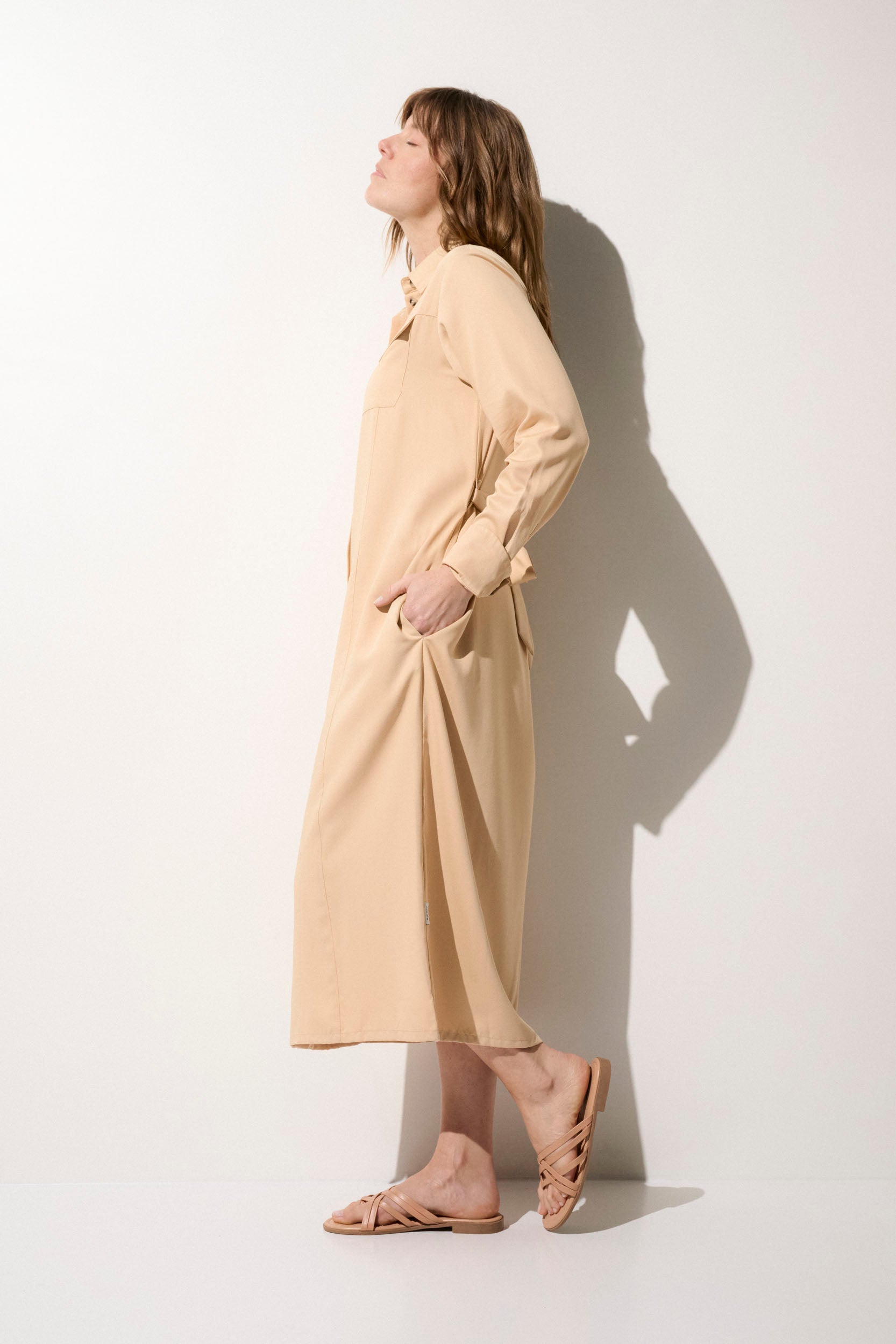 Femme portant une robe-chemise anti-UV beige, UPF50+, élégante pour une sortie en bord de mer.