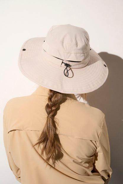 Chapeau anti-UV beige UPF50+ porté par une femme, idéal pour protection solaire lors de randonnées.