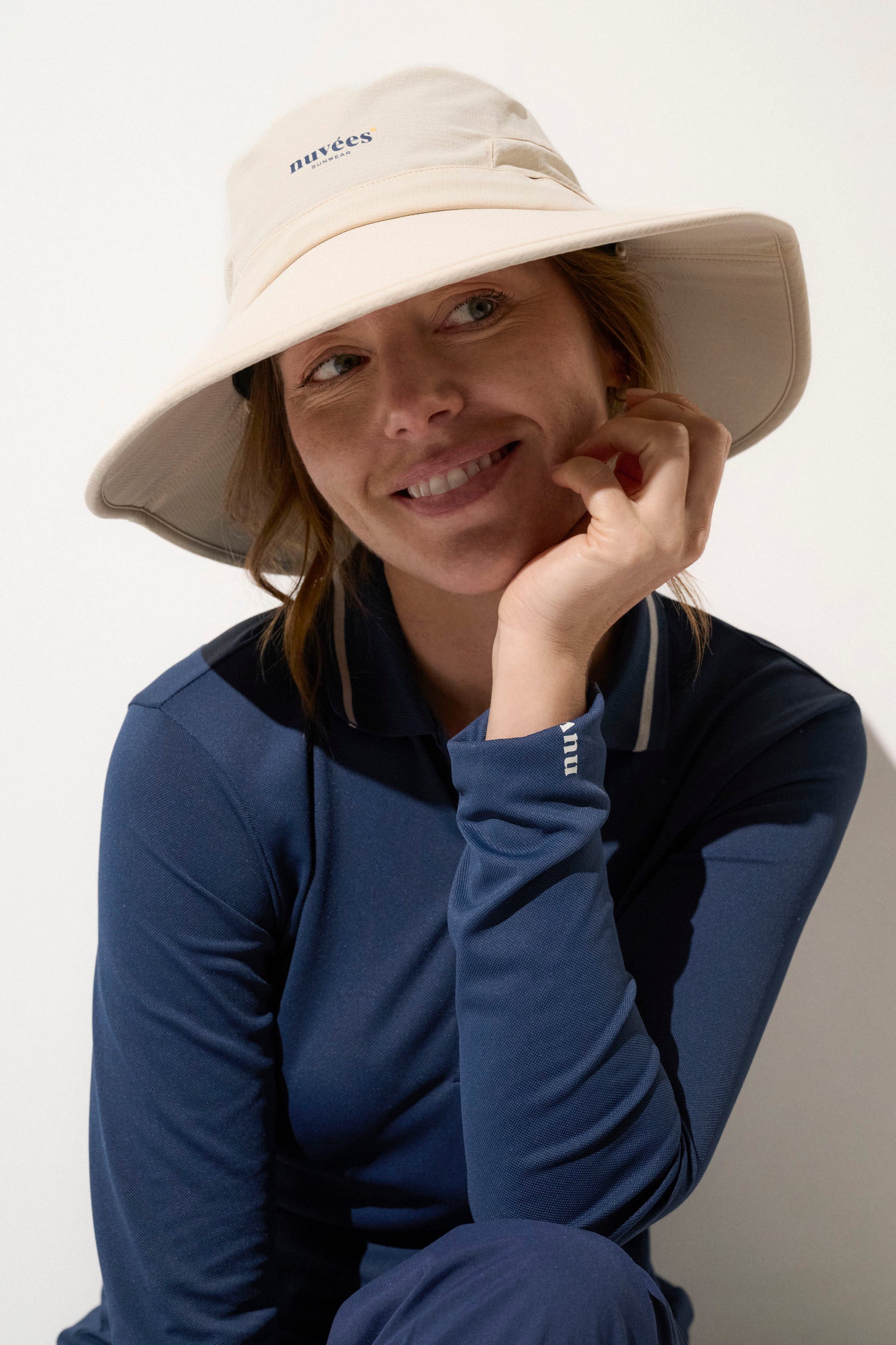 Femme souriante portant un chapeau anti-UV beige avec logo Nuvées, idéal pour le golf et les activités en plein air.