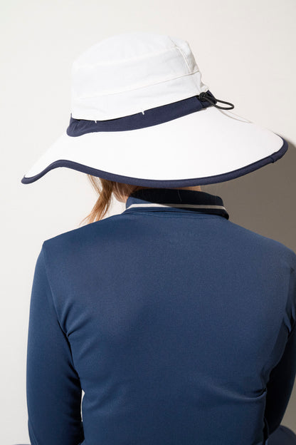 Chapeau anti-UV blanc et bleu UPF50+ porté par une femme, idéal pour le golf et d'autres sports de plein air.