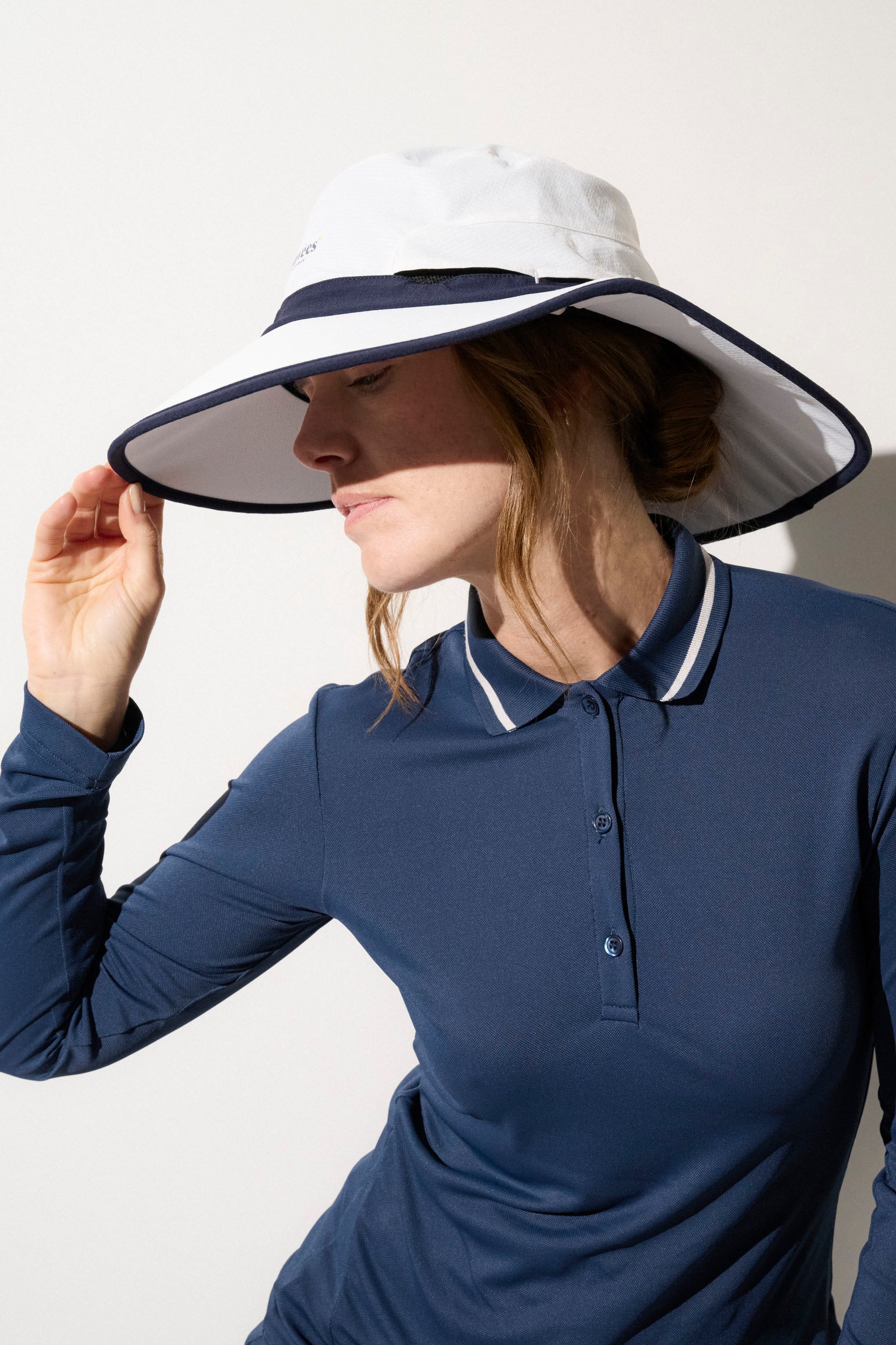 Femme portant un chapeau anti-UV blanc et bleu, conçu pour le golf, avec protection UPF50+.