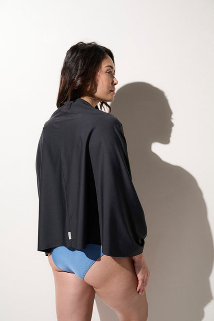 Femme portant une veste anti-UV noire UPF 50+ avec un maillot de bain bleu, idéale pour la protection solaire.