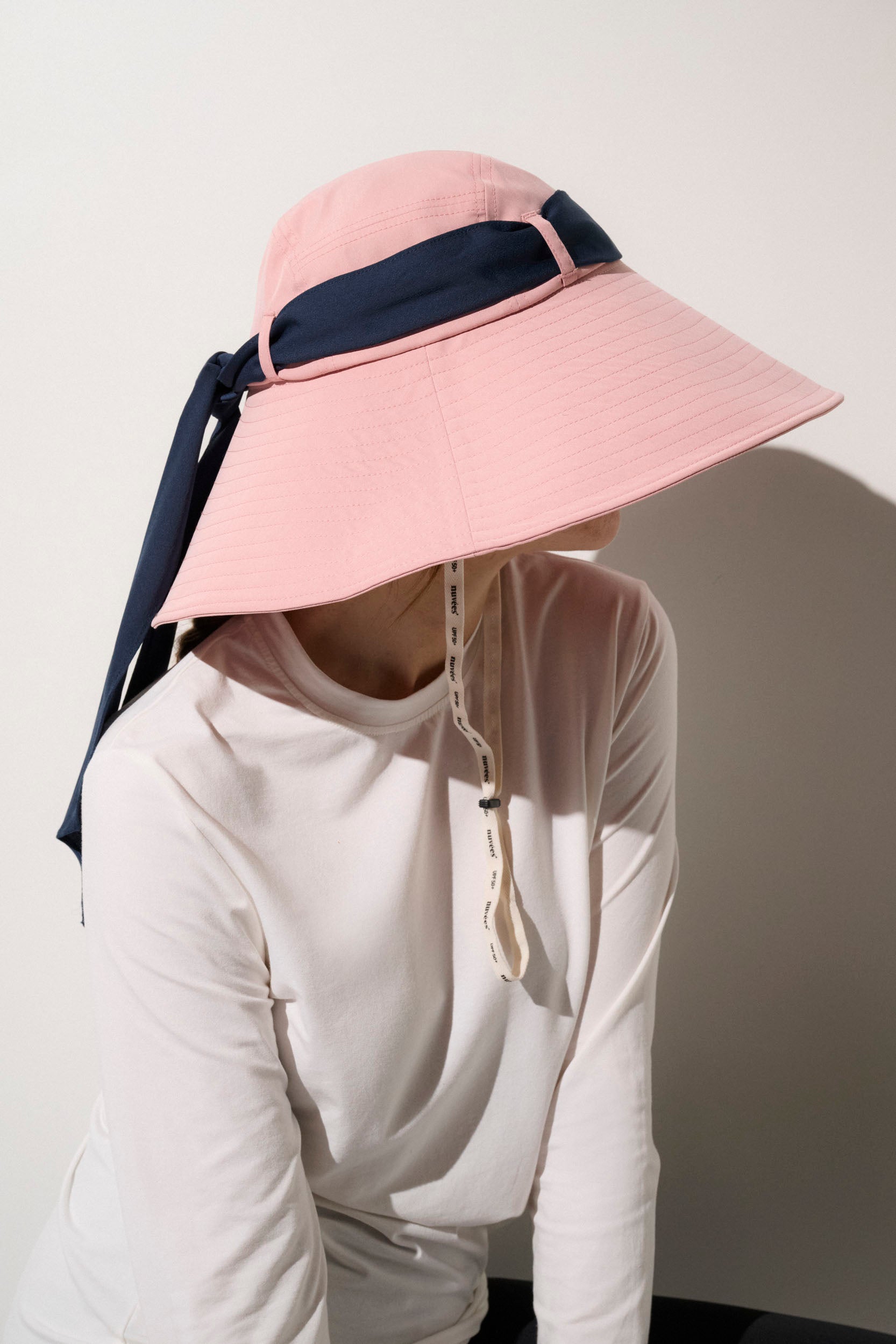 Chapeau anti-UV rose avec bande navy, protection solaire UPF50+, porté par femme en tenue décontractée.