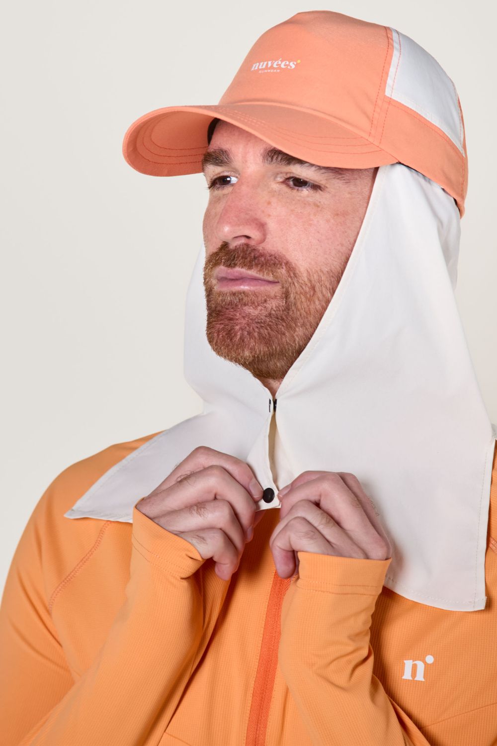 Homme portant une casquette anti-UV orange Nuvées avec protection solaire attachée, idéale pour les activités extérieures.