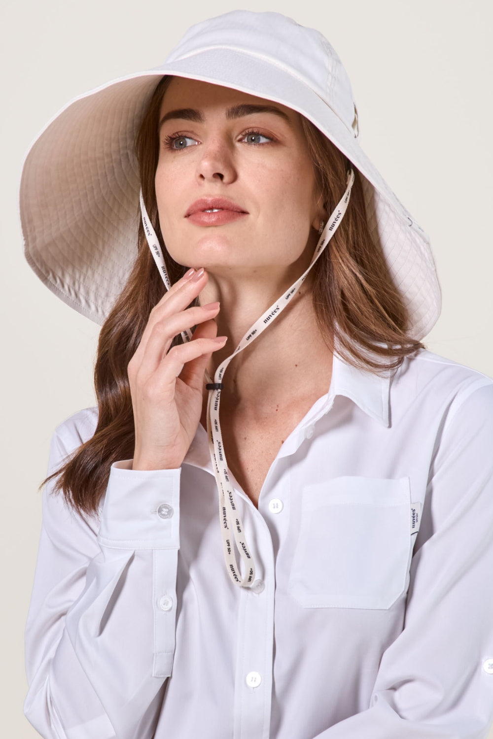 Femme portant un chapeau anti-UV blanc, élégant, avec large bord pour une protection solaire optimale.