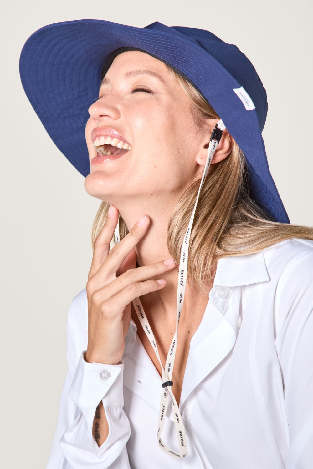 Femme souriante portant un chapeau anti-UV bleu, idéal pour une protection solaire élégante.