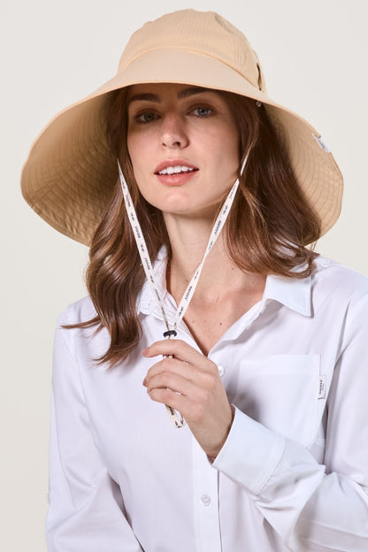 Femme souriante portant un chapeau anti-UV beige avec jugulaire, idéal pour la protection solaire.