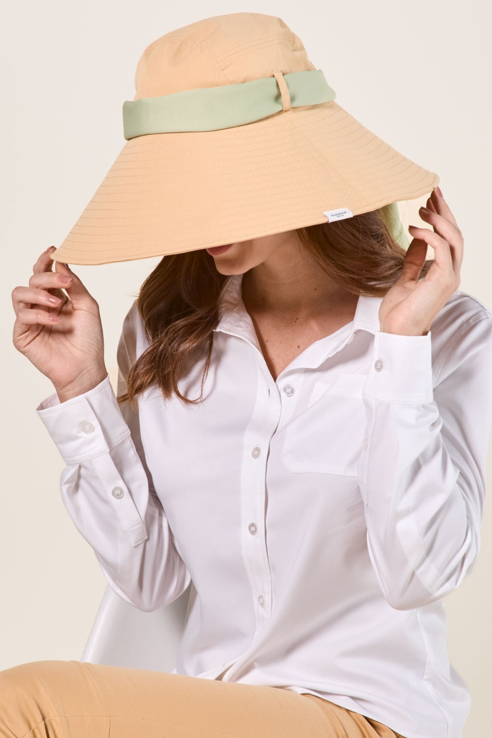 Chapeau anti-UV beige avec bande verte, en couleur Café Glacé, porté par une femme pour protection solaire élégante.