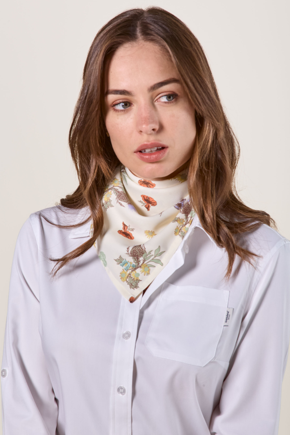 Foulard anti-UV pour femme, motif fleuri délicat, UPF 50+, porté autour du cou avec une chemise blanche.