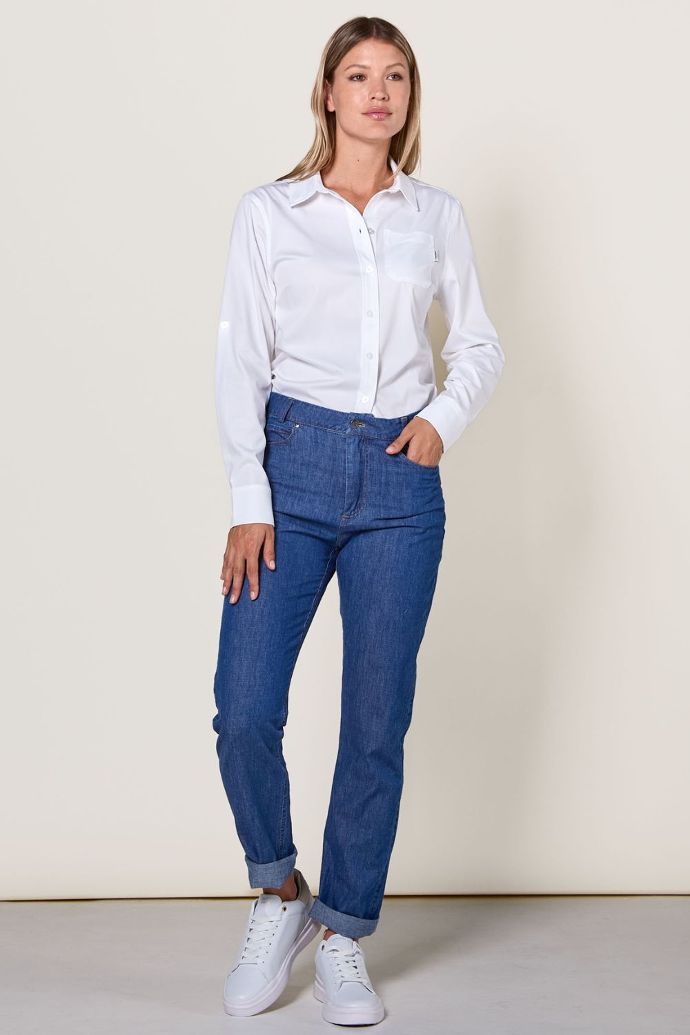 Femme portant une chemise blanche et un pantalon anti-UV bleu, certifié UPF 50+, au style décontracté et élégant.