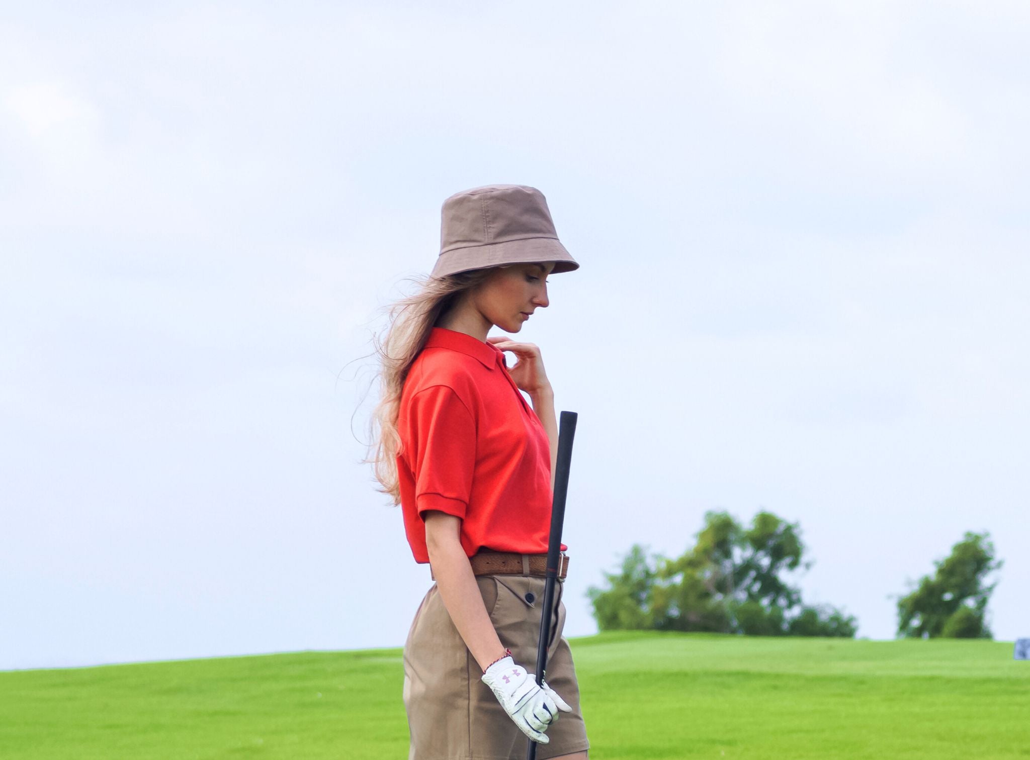 Femme sur un green de golf et portant un bob et un polo anti-UV