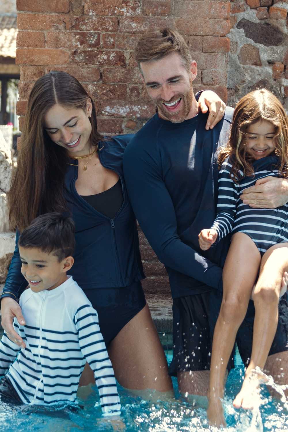 Famille en vêtements anti-UV allant de haut en bas, à rayures et unis, jouant dans une piscine, protection solaire UPF50+.