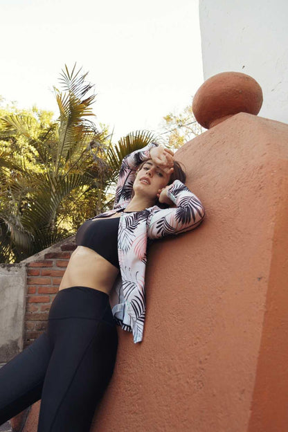 Femme portant un legging de bain anti-UV noir et une veste légère à motifs, protégeant du soleil en extérieur.