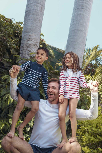 Homme portant un t-shirt anti-UV blanc UPF50+ avec deux enfants en maillots rayés, idéal pour se protéger au soleil.