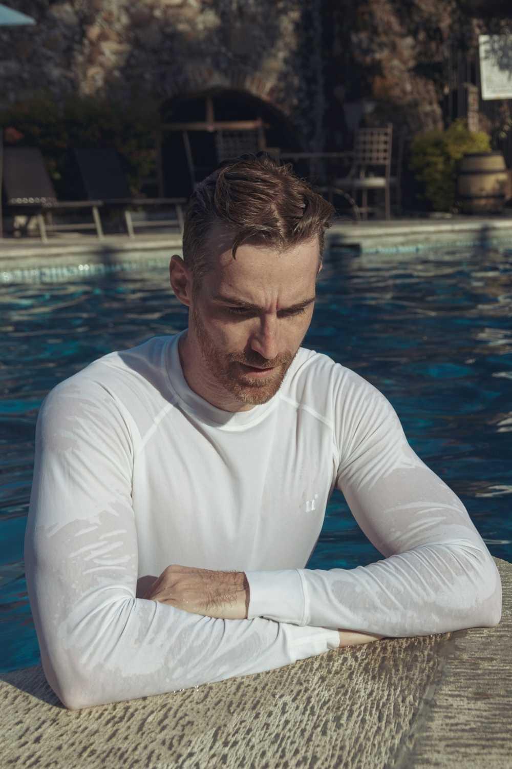 Homme portant un t-shirt anti-UV blanc UPF 50+ au bord d'une piscine, idéal pour la baignade.